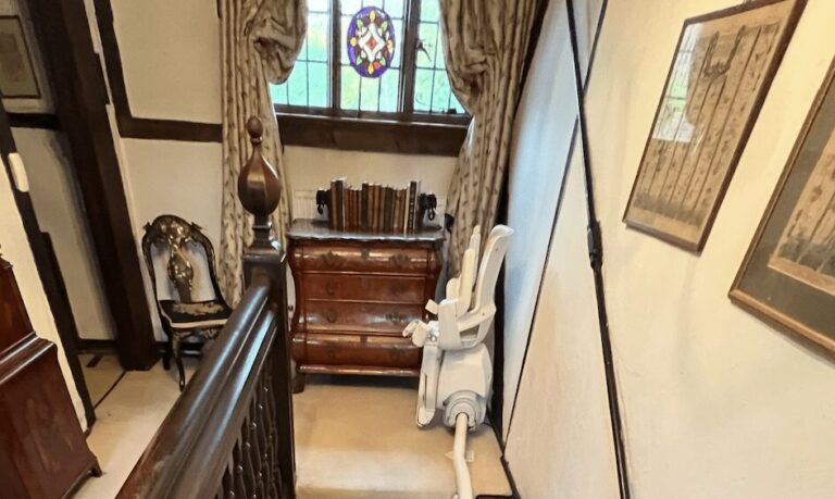 Curved Stairlift Model on Straight Stairs - Case Study (Otolift Modul-Air Smart) - Kudos Stairlifts blog header image, stairlift at top of stairs with seat folded